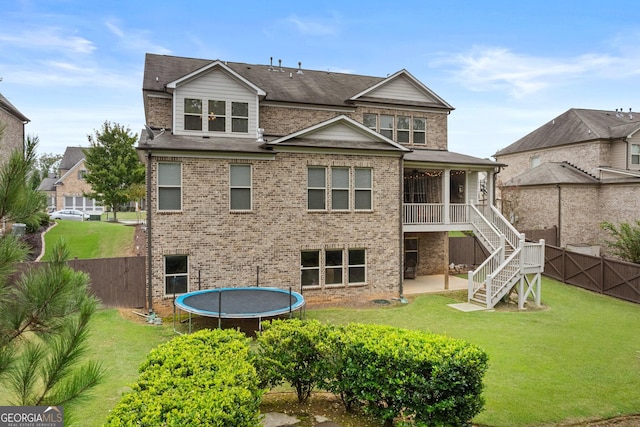 back of property with brick siding, a trampoline, stairs, a yard, and a patio