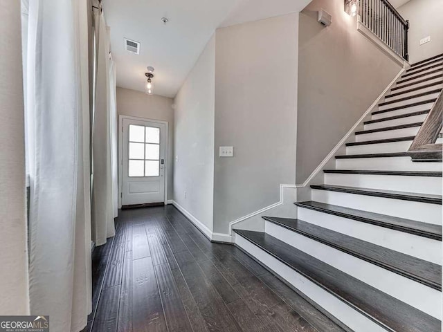 foyer entrance with dark wood finished floors, visible vents, stairway, and baseboards