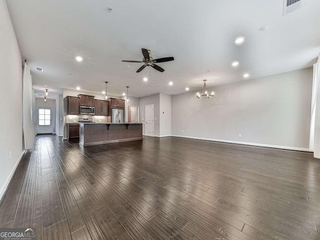 unfurnished living room with dark wood-type flooring, recessed lighting, ceiling fan with notable chandelier, and baseboards