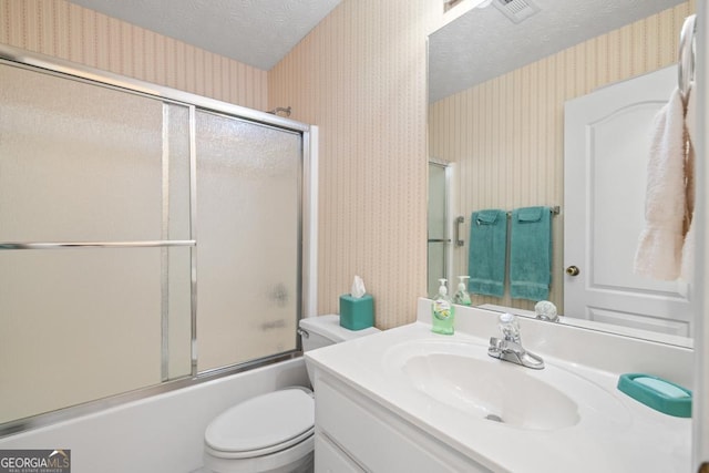 bathroom featuring wallpapered walls, toilet, vanity, combined bath / shower with glass door, and a textured ceiling