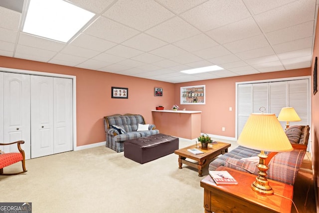 carpeted living area featuring baseboards and a drop ceiling