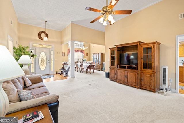 carpeted living room with visible vents, ornamental molding, a textured ceiling, a high ceiling, and ornate columns