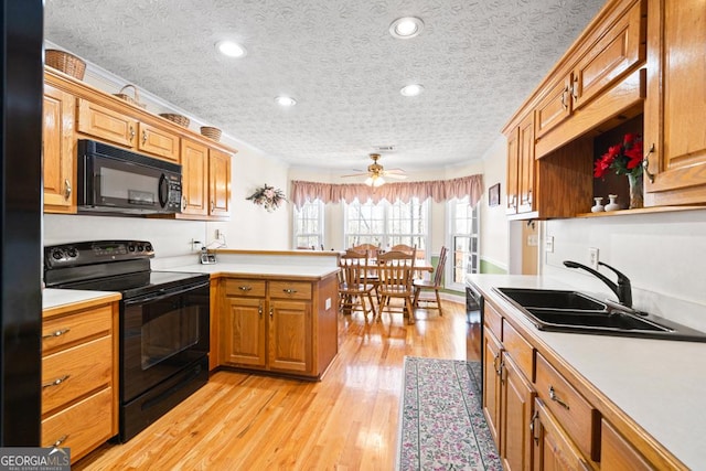 kitchen with a peninsula, a sink, black appliances, light countertops, and light wood-type flooring