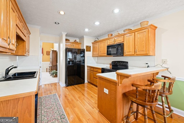 kitchen featuring a breakfast bar, a peninsula, light wood-style flooring, a sink, and black appliances