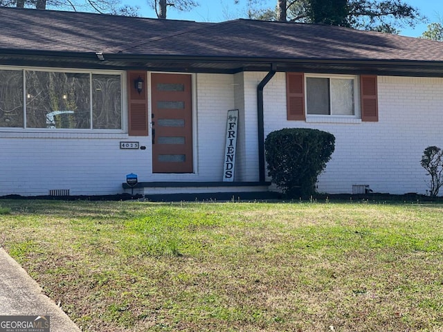 view of exterior entry featuring a lawn, brick siding, roof with shingles, and crawl space