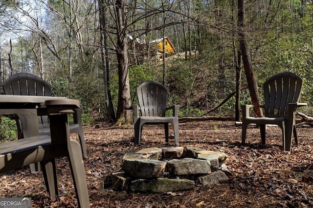 view of community featuring a wooded view and an outdoor fire pit