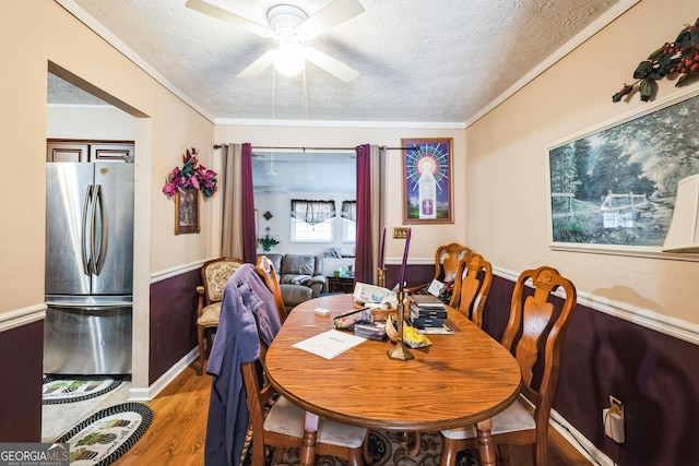 dining area featuring light wood-style flooring, a textured ceiling, crown molding, and ceiling fan