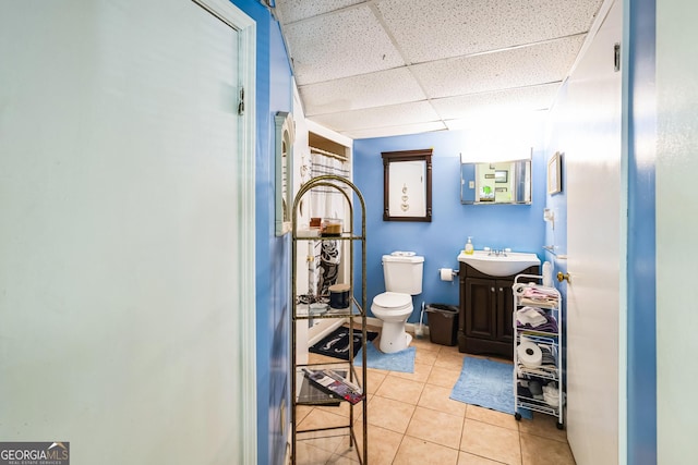 half bathroom with tile patterned flooring, toilet, vanity, and a drop ceiling