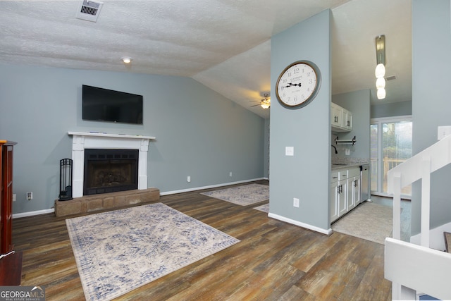 living room featuring a tiled fireplace, lofted ceiling, visible vents, and dark wood-type flooring