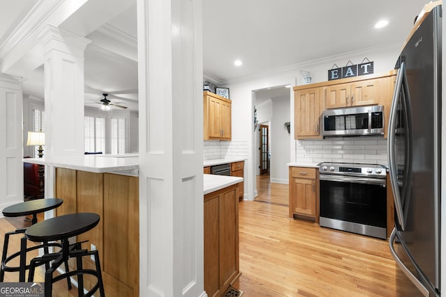 kitchen with a breakfast bar, light wood-type flooring, ornamental molding, decorative columns, and appliances with stainless steel finishes