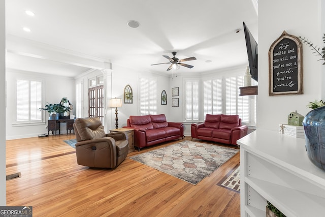 living area with a wealth of natural light, visible vents, light wood-style flooring, and decorative columns