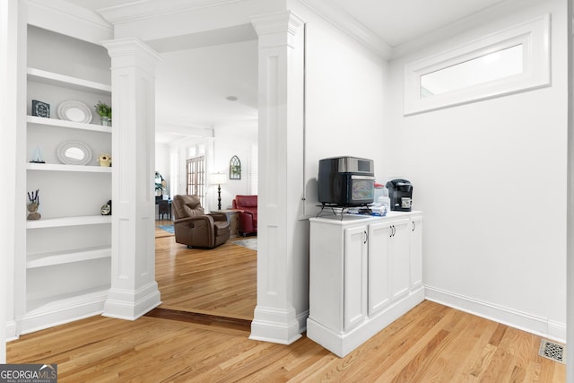 interior space featuring visible vents, built in shelves, ornamental molding, light wood-style floors, and ornate columns