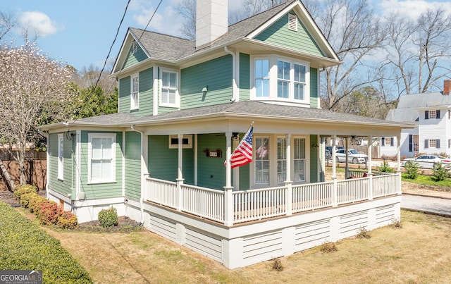 view of front of house featuring a shingled roof, a front yard, covered porch, and a chimney