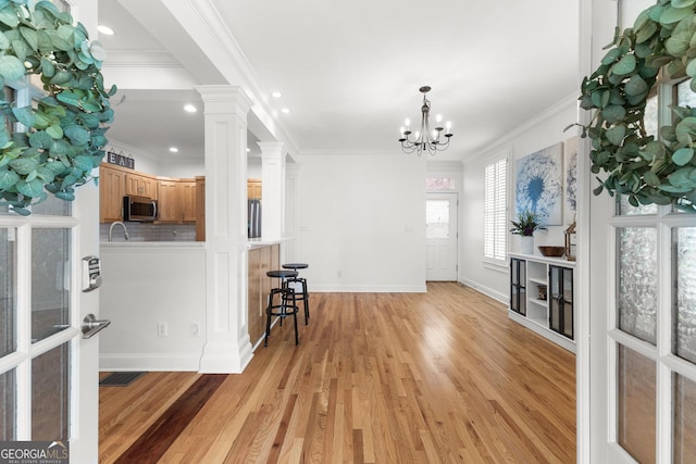 foyer entrance with light wood-type flooring, baseboards, crown molding, and ornate columns