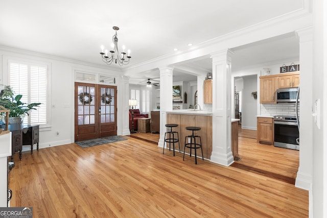 entrance foyer with decorative columns, ornamental molding, french doors, ceiling fan with notable chandelier, and light wood-type flooring