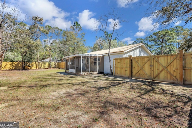 back of house featuring a gate, a fenced backyard, a sunroom, a lawn, and brick siding