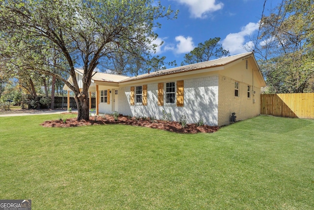 ranch-style home featuring a front yard, fence, brick siding, and metal roof