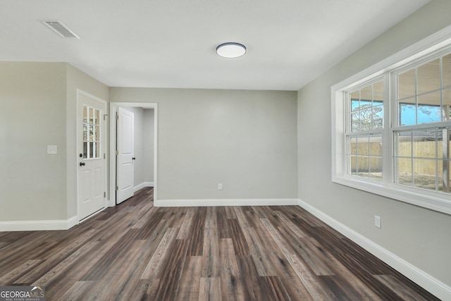 empty room with dark wood finished floors, baseboards, and visible vents