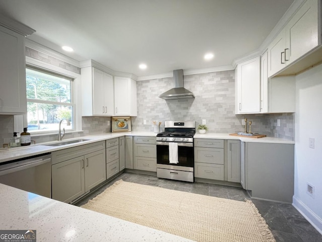 kitchen featuring gray cabinets, a sink, tasteful backsplash, appliances with stainless steel finishes, and wall chimney range hood