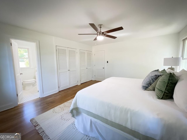 bedroom with two closets, ensuite bathroom, a ceiling fan, wood finished floors, and baseboards