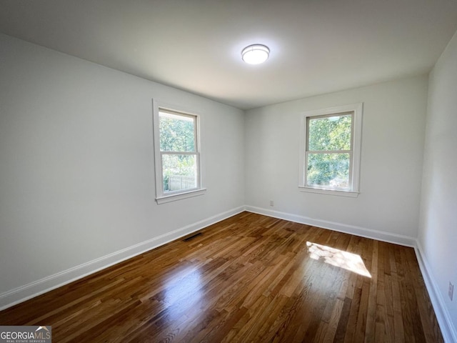 spare room featuring dark wood-style floors, a healthy amount of sunlight, and baseboards