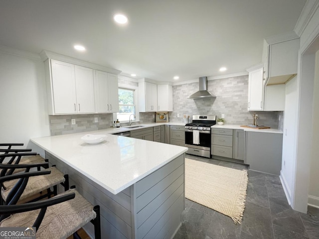 kitchen with wall chimney range hood, a kitchen breakfast bar, stainless steel appliances, a peninsula, and light countertops