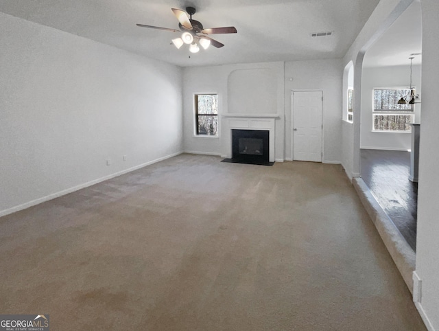 unfurnished living room with a ceiling fan, visible vents, baseboards, carpet floors, and a fireplace with flush hearth