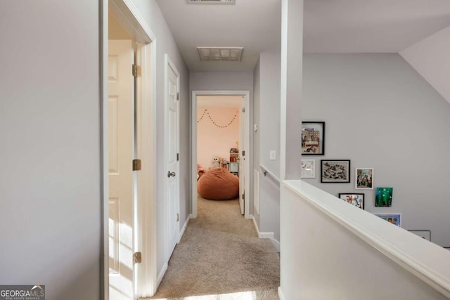 hallway with visible vents, an upstairs landing, carpet, and baseboards