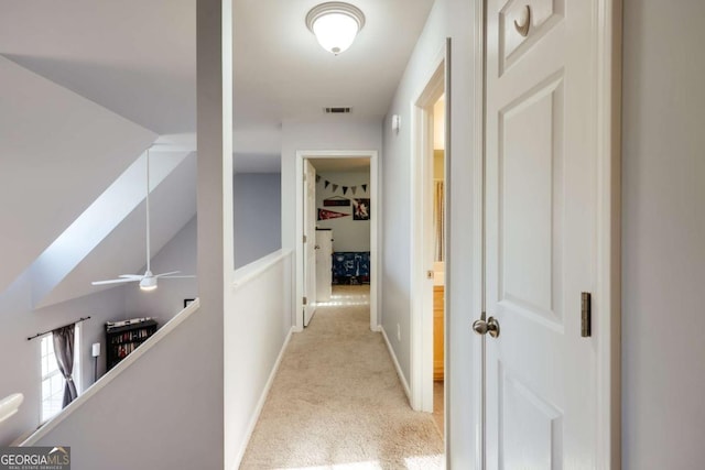 hall with an upstairs landing, visible vents, light colored carpet, and baseboards