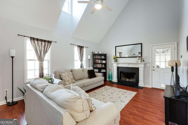 living area with a fireplace, wood finished floors, baseboards, and high vaulted ceiling