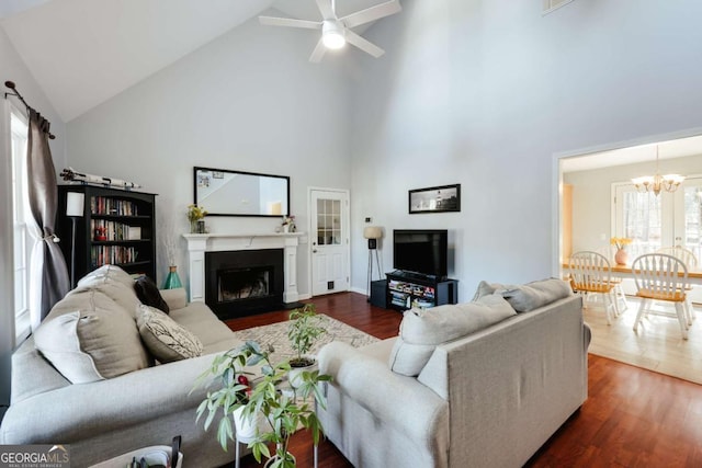 living area with ceiling fan with notable chandelier, a fireplace, high vaulted ceiling, and dark wood-type flooring