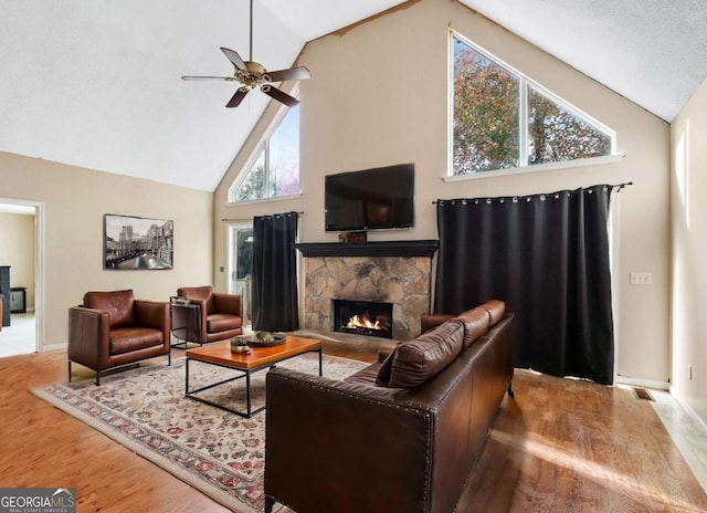 living room with visible vents, a stone fireplace, wood finished floors, high vaulted ceiling, and a ceiling fan