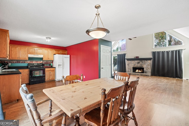 dining area with a fireplace, light wood-type flooring, and lofted ceiling