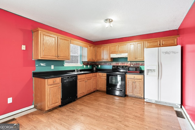 kitchen featuring a sink, black appliances, light wood-style floors, under cabinet range hood, and dark countertops