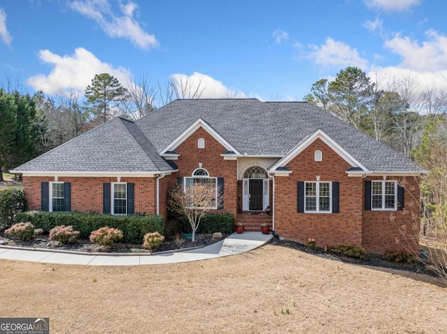 view of front facade featuring brick siding, a front yard, and a shingled roof