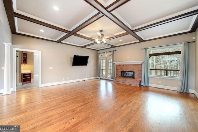 unfurnished living room featuring light wood-type flooring, coffered ceiling, baseboards, a brick fireplace, and ornate columns