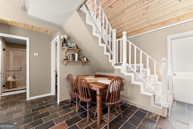 dining space featuring stairway, stone tile floors, wood ceiling, and baseboards