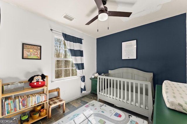 bedroom featuring visible vents, a ceiling fan, stone tile flooring, a nursery area, and baseboards