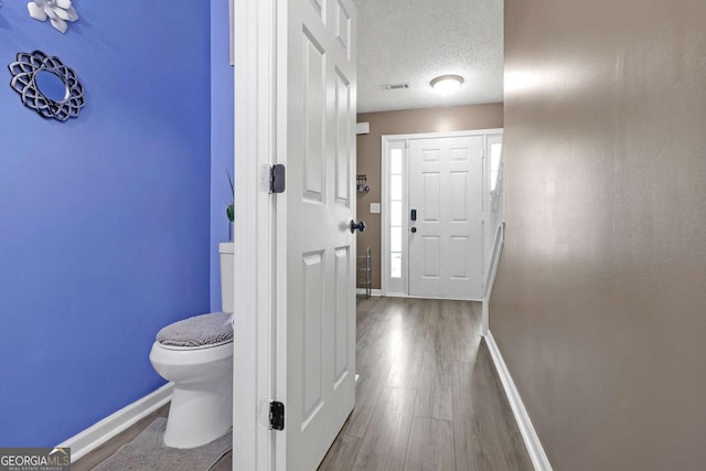 hallway featuring visible vents, baseboards, a textured ceiling, and wood finished floors