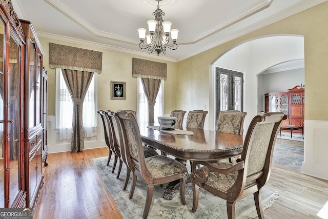 dining space with arched walkways, a chandelier, light wood finished floors, and ornamental molding