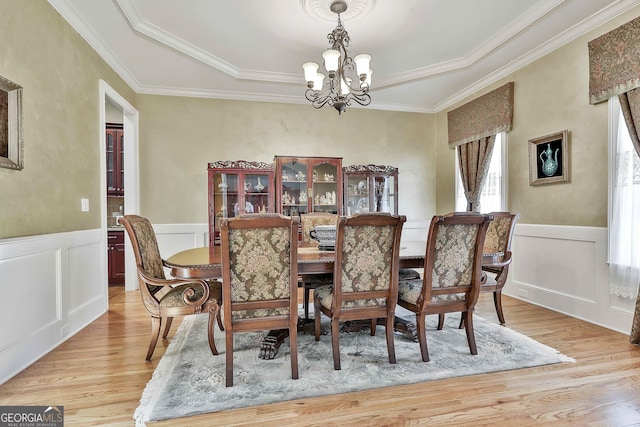 dining space with ornamental molding, a notable chandelier, light wood finished floors, and wainscoting