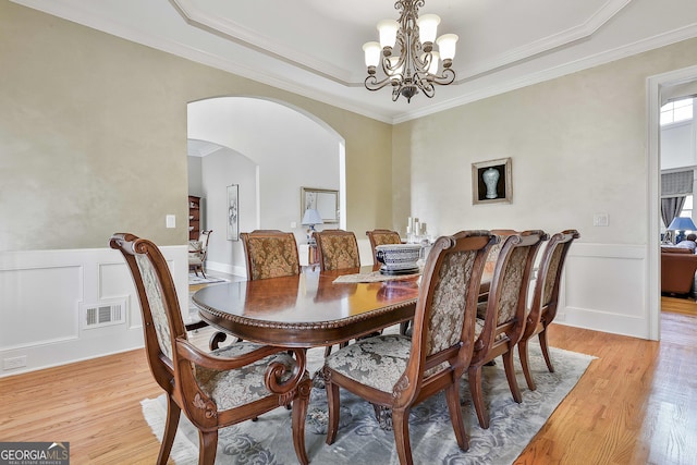 dining room with visible vents, light wood-type flooring, wainscoting, arched walkways, and a notable chandelier