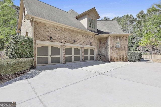 view of side of home featuring brick siding, concrete driveway, a garage, and roof with shingles