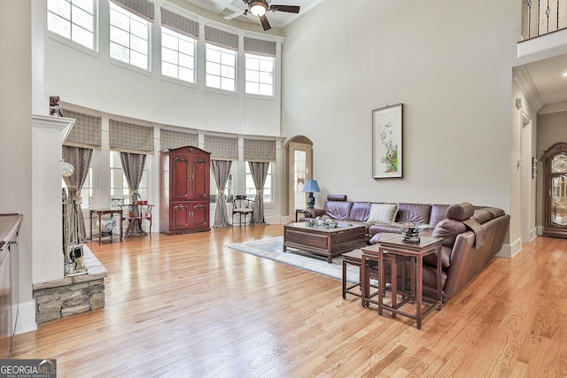 living area with arched walkways, crown molding, ceiling fan, and wood finished floors