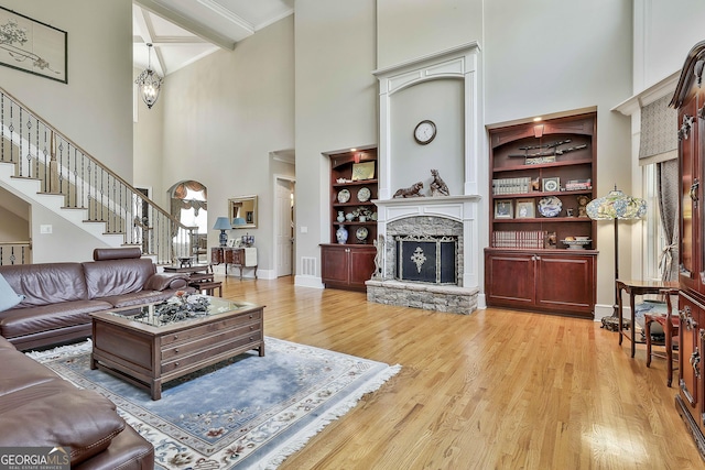 living room featuring visible vents, built in shelves, light wood-style floors, a stone fireplace, and stairs