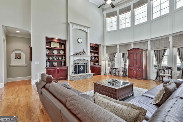 living area featuring visible vents, a high ceiling, a fireplace, crown molding, and light wood-type flooring