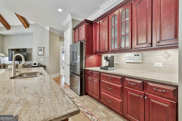 kitchen featuring a sink, backsplash, freestanding refrigerator, reddish brown cabinets, and light stone countertops