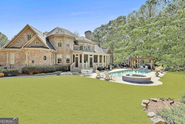 rear view of property featuring brick siding, a pool with connected hot tub, a lawn, a sunroom, and a patio