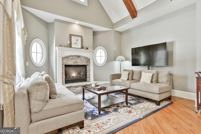 living area with a stone fireplace, baseboards, a healthy amount of sunlight, and wood finished floors