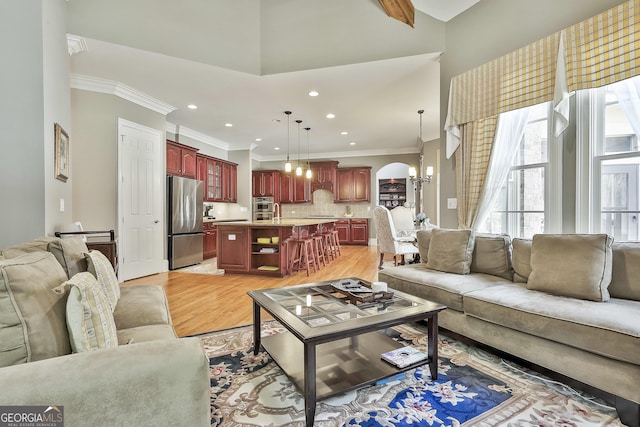 living area with crown molding, a chandelier, a high ceiling, light wood-style floors, and arched walkways